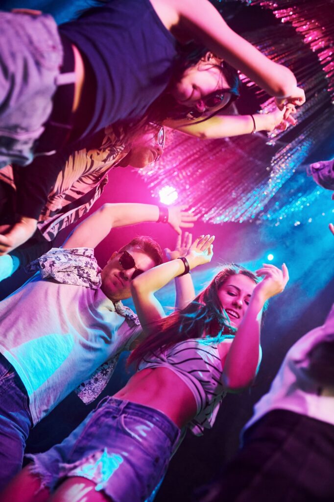 View from below of young people that having fun in night club with colorful laser lights